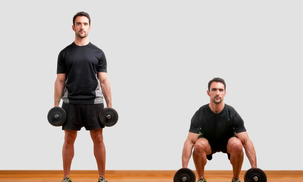 Man wearing black T-shirt doing dumbbell squat exercise on wooden floor