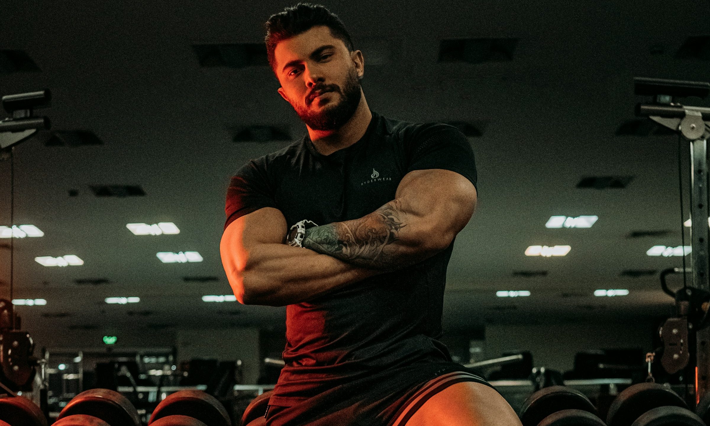 Strong man standing in the gym arms folded leaning on weight rack