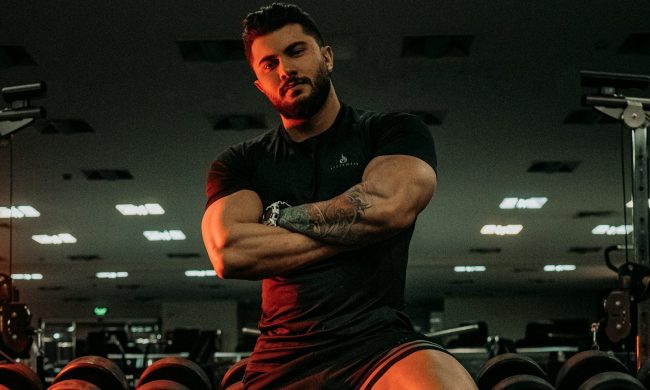Strong man standing in the gym arms folded leaning on weight rack