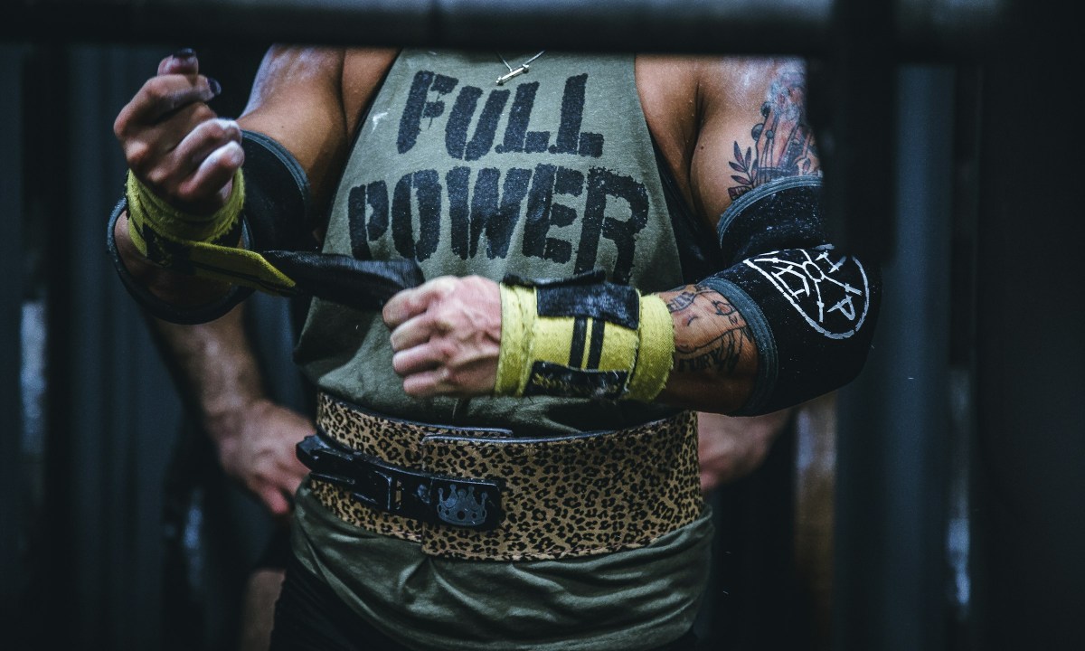 Close-up of a man wearing Full Power shirt putting gloves on wearing training belt gym weightlifting