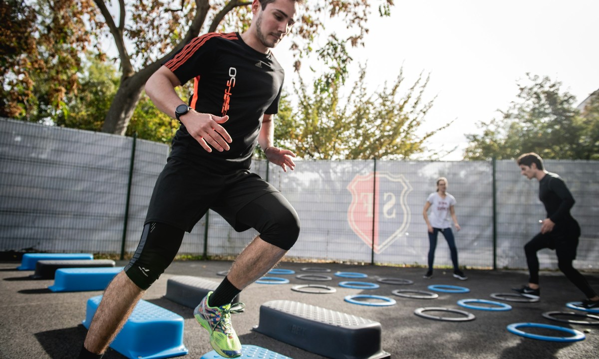 man wearing black t shirt exercising outdoors outside with blue steps