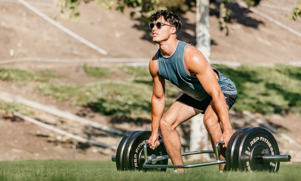 Man outside wearing blue sleeveless shirt doing trap bar deadlift in nature