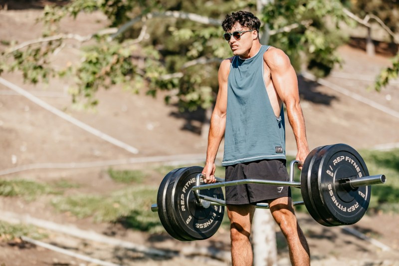 Man outside wearing sleeveless shirt in nature doing trap bar deadlift hex bar