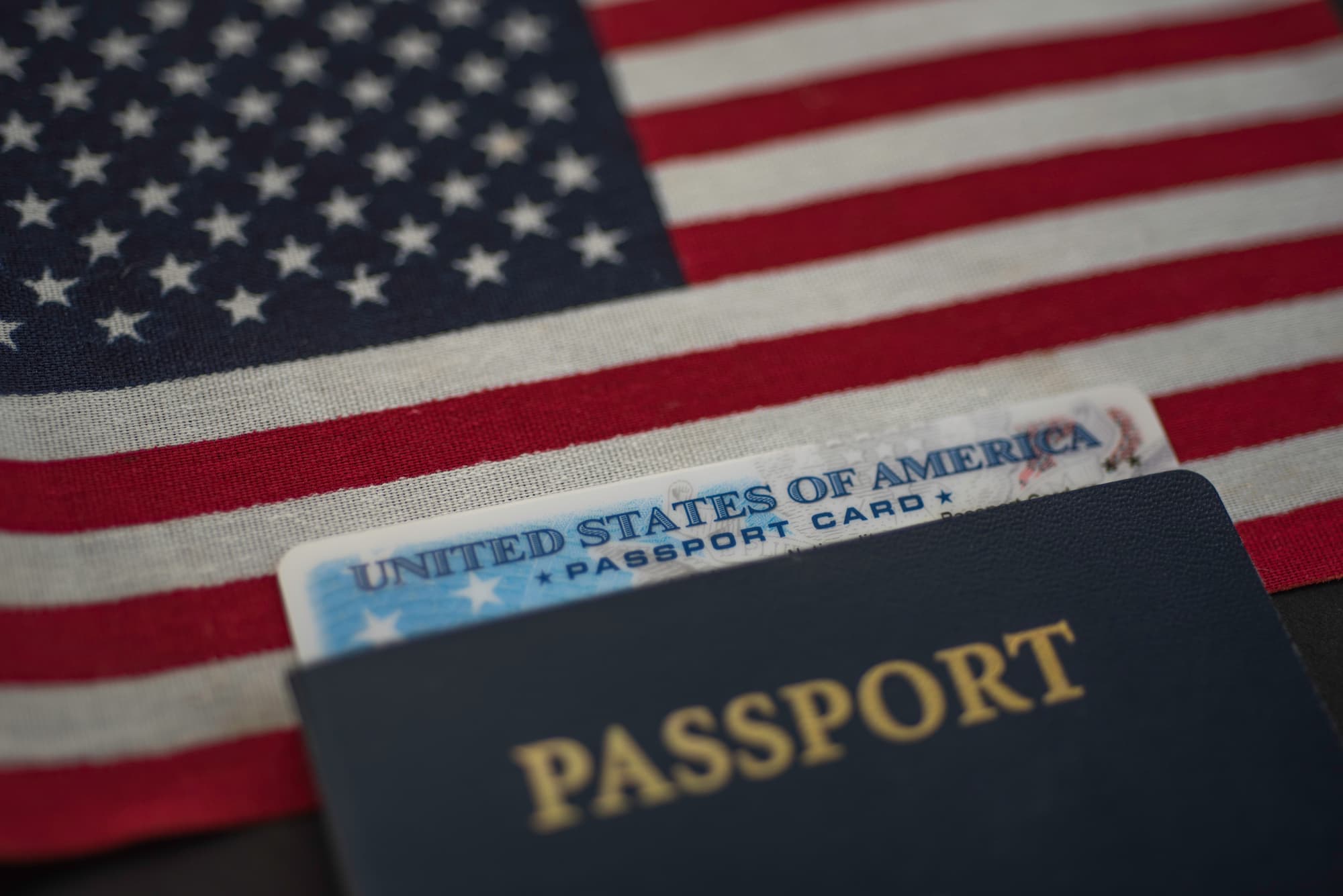 U.S. passport card inside passport book with an American flag in the background