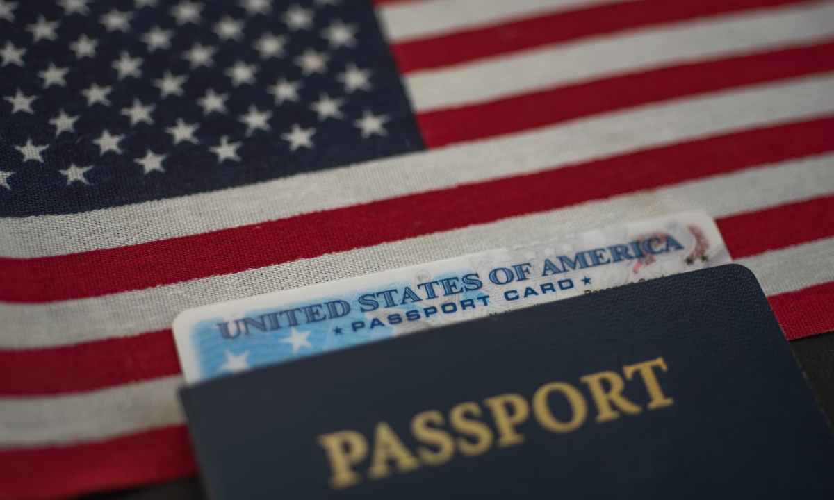 U.S. passport card inside passport book with an American flag in the background