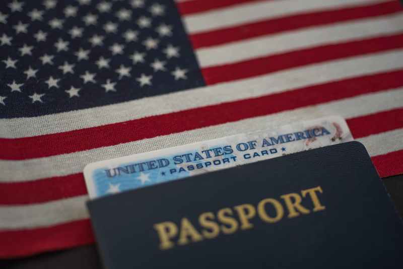U.S. passport card inside passport book with an American flag in the background