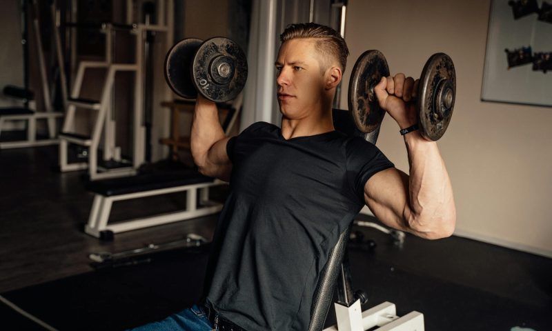 Man with black t shirt doing arnold press dumbbell press exercise in gym