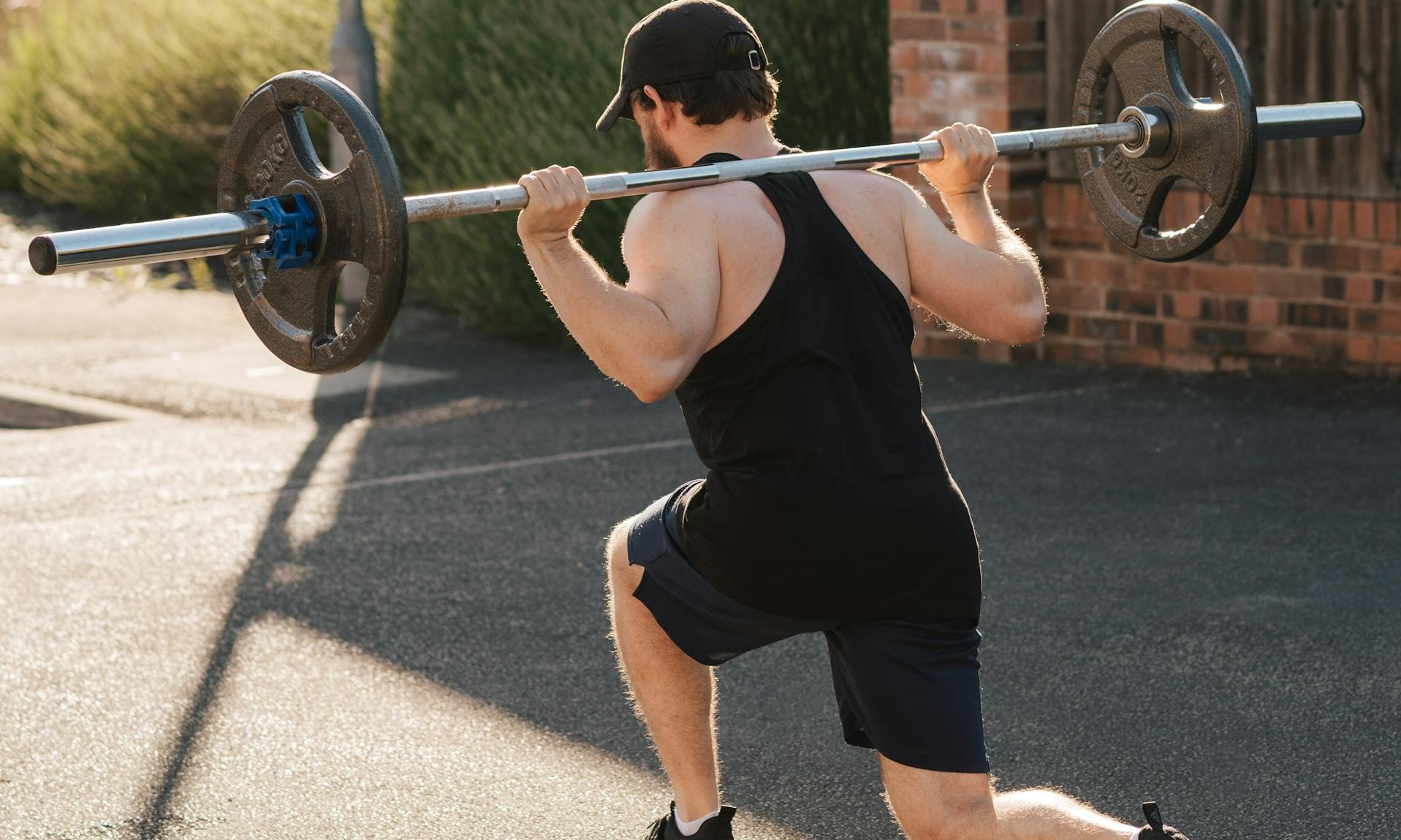 Man doing barbell lunge outside brick wall