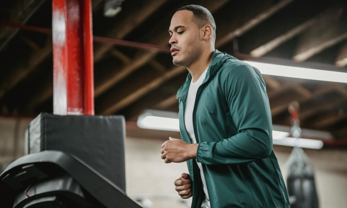 Man running on treadmill wearing blue jacket in gym