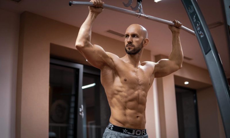 shirtless muscular man ripped in gym holding lat pulldown bar standing up ready to exercise at home