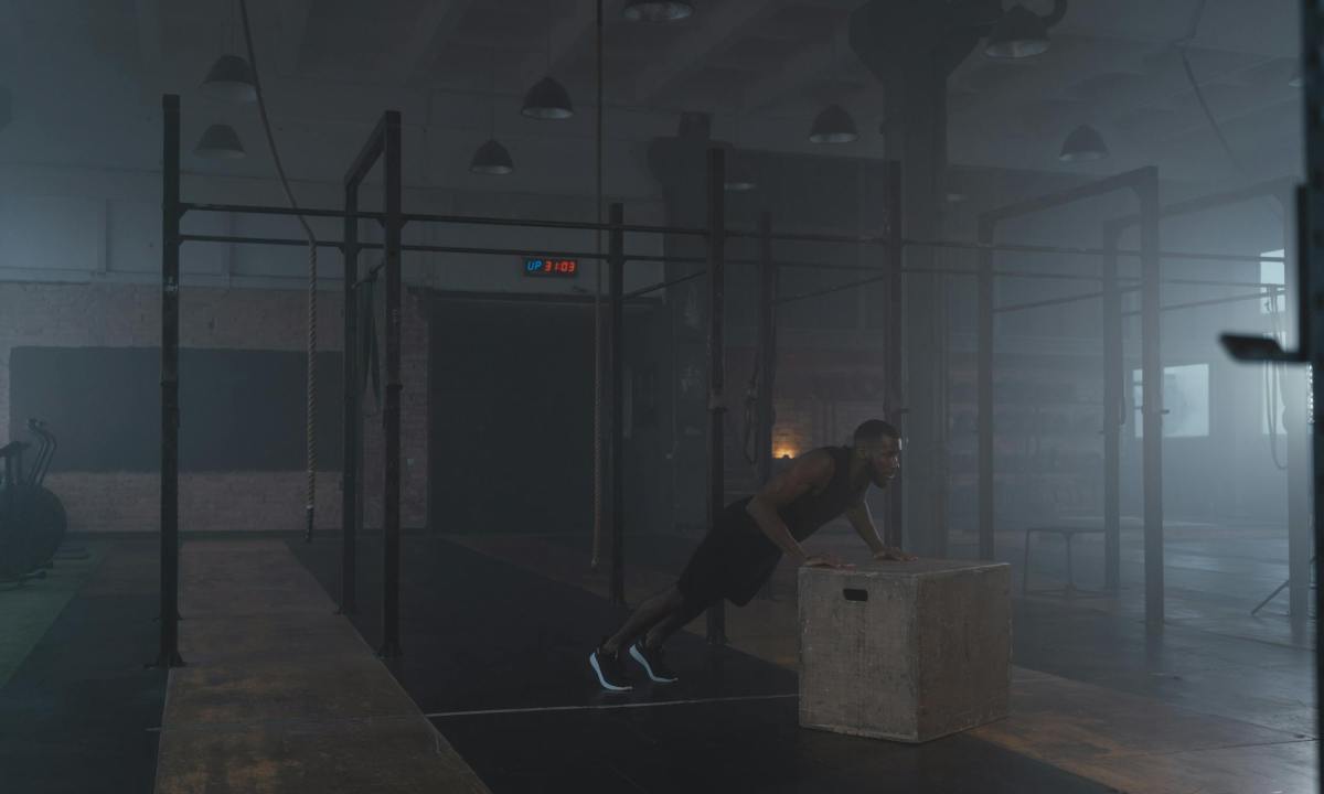 man doing incline push up in gym on wooden plyo box dark room