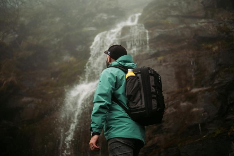 Man wearing green and hat rucking backpack rucksack walking in nature by waterfall with drink water