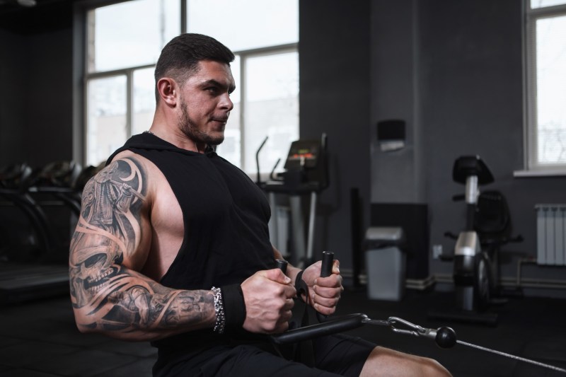 Man with tattoos sitting in the gym doing seated cable rows exercise with cable machine