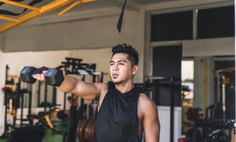 man doing one arm dumbbell front raise exercise in gym