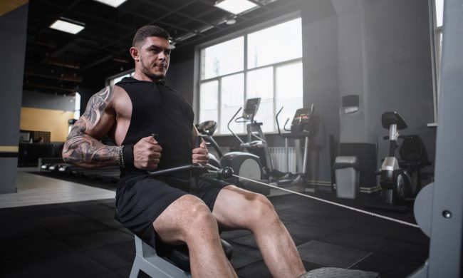 Man sitting in gym doing seated cable row on cable machine