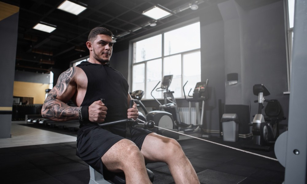 Man sitting in gym doing seated cable row on cable machine