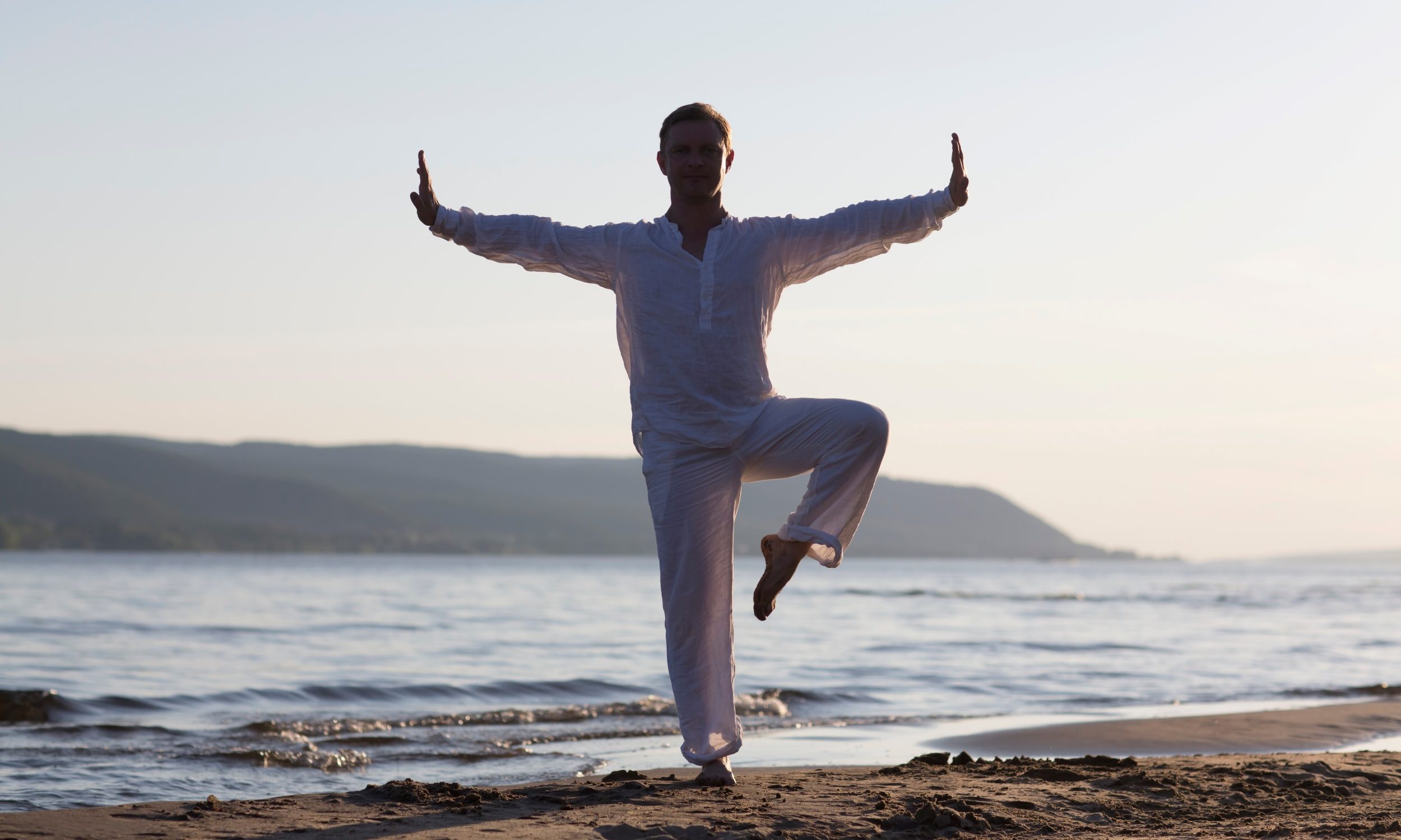 man wearing white on the beach performing Qigong martial arts training tai chi movement stretching