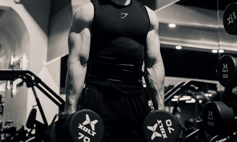 Man in gym black and white pic holding dumbbells down at his sides ready to do dumbbell squat exercise in gym