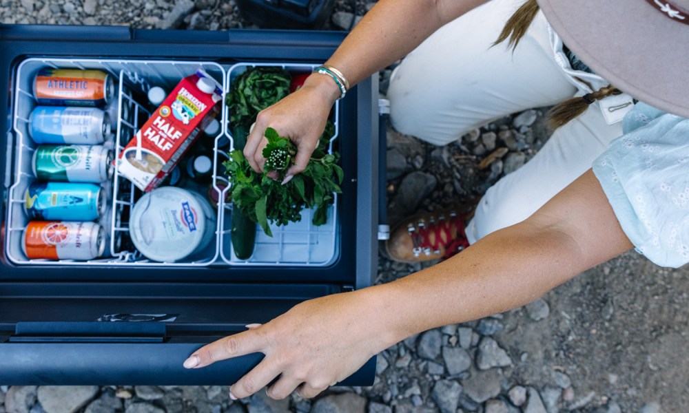 Young woman removing fresh herbs from a Dometic CFX5 series electric cooler.