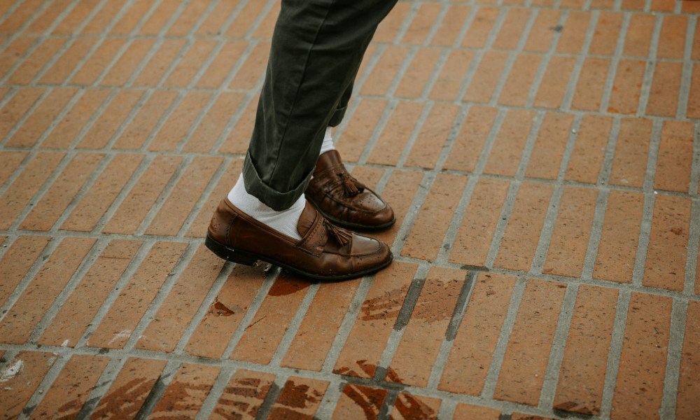 person wearing brown leather shoes on bricks