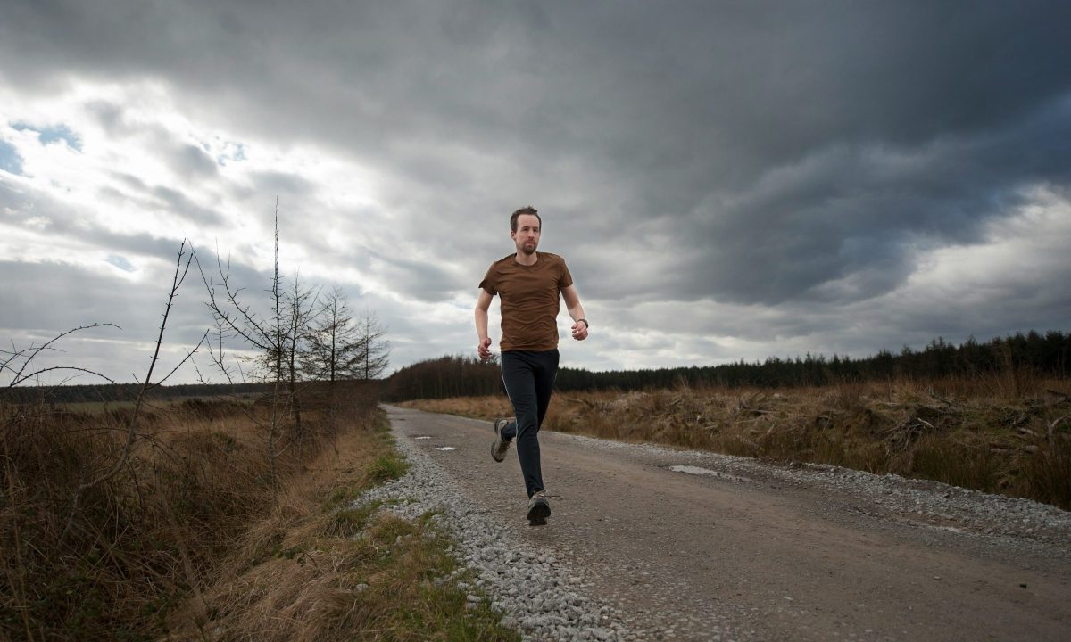man running outside grey clouds on road