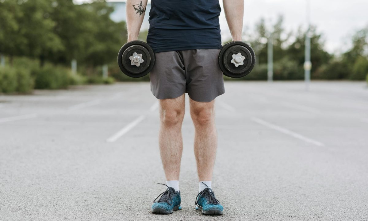 man doing dumbbell shrug holding dumbbells outside standing in parking lot