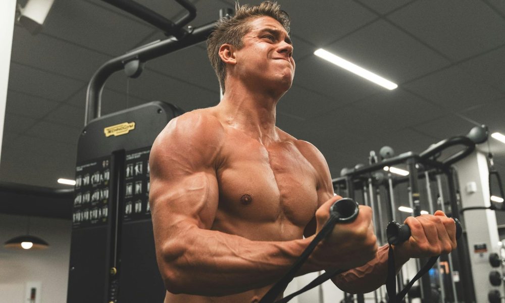 man shirtless muscle flex doing cable bicep curl in gym on cable machine