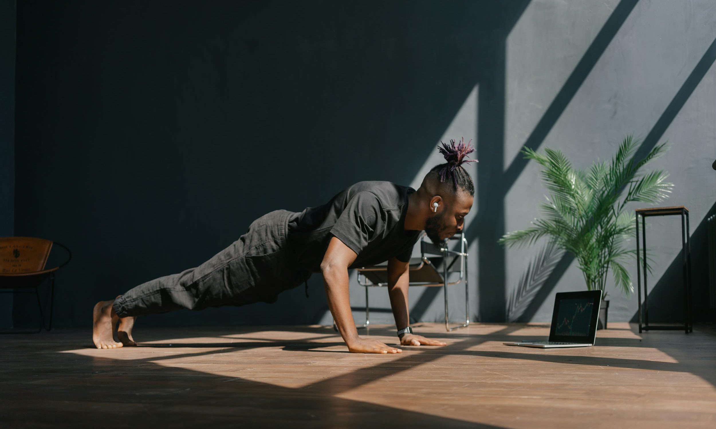Man working with remote personal trainer doing virtual exercise class at home working out yoga plank pushup