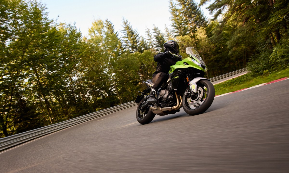 2025 Triumph Tiger Sport 660 making a sweeping left turn on a racetrack with trees in the background.