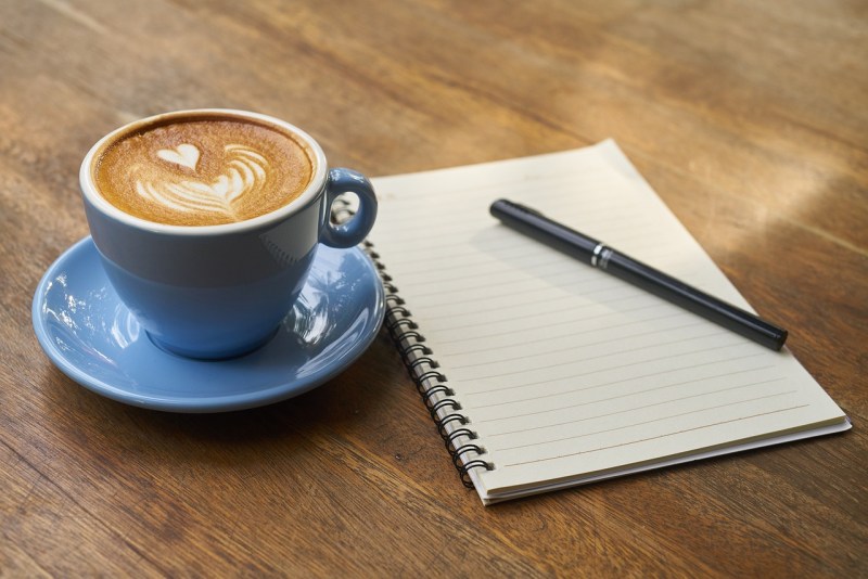 Latte next to a pad of paper and a pen