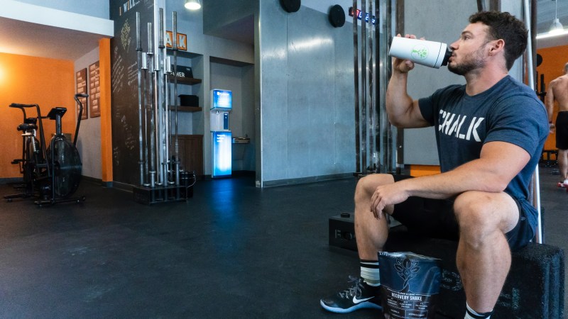 man in gym sitting on bench drinking protein shake or creatine supplement