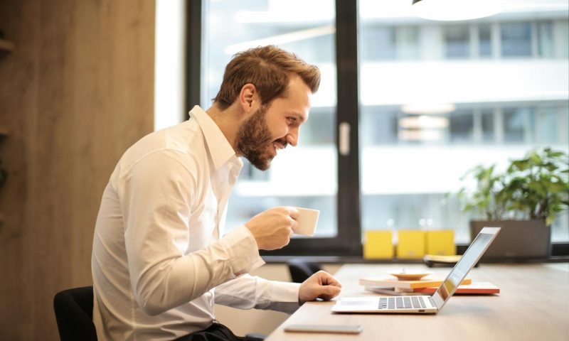 man smiling drinking tea working at desk
