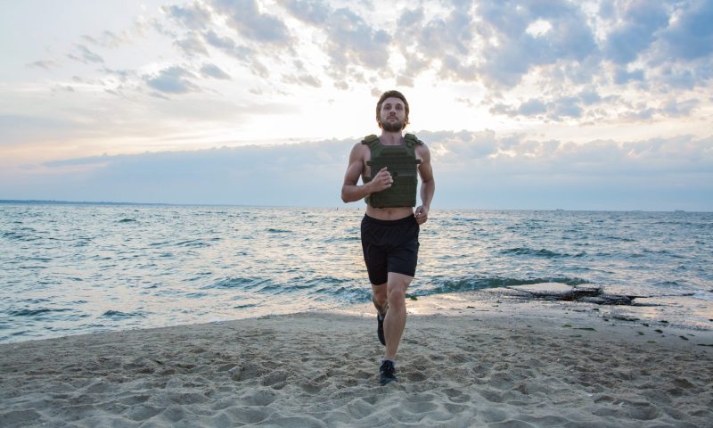 Man walking jogging running wearing weighted vest outdoors beach workout