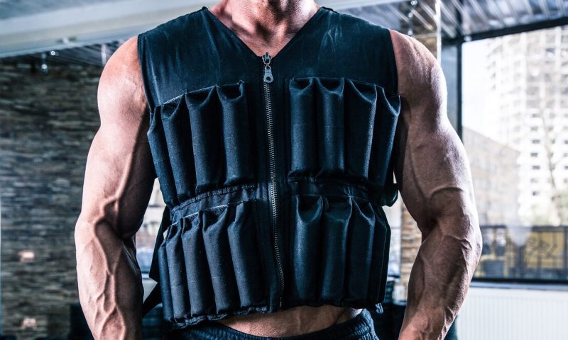 man wearing weighted vest in gym close up arms muscular muscles flex fist clench