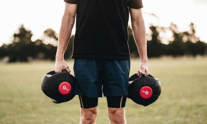 man outside on grass holding weights dumbbells