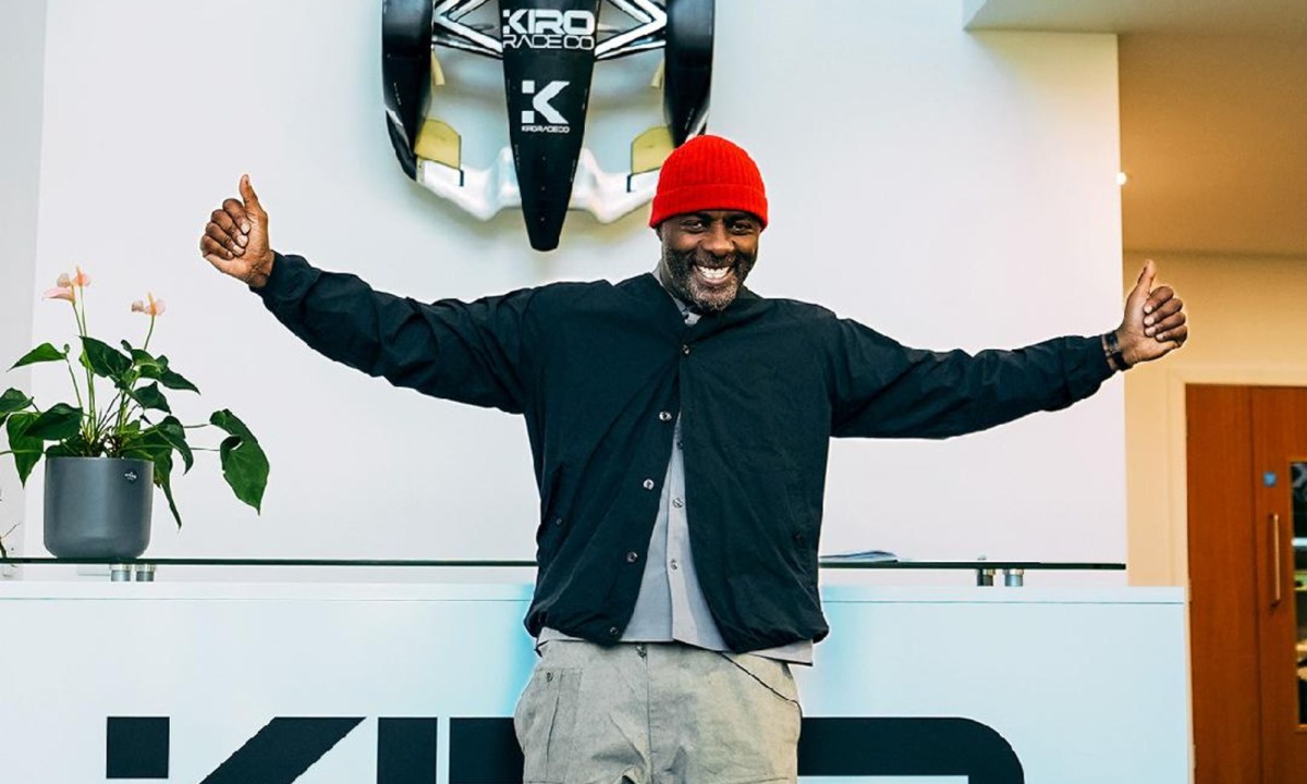 Idris Elba psoign with arms out in front of a Kiro Race co race car model.