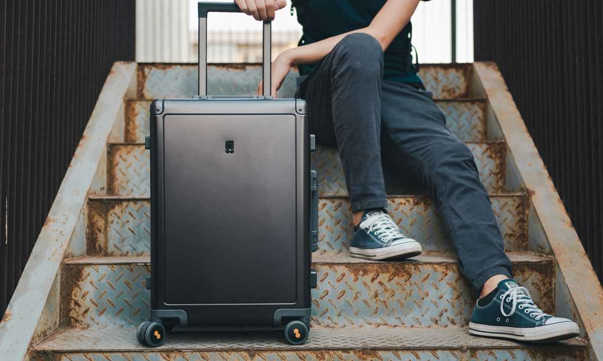 person sitting on stairs with a black rolling suitcase
