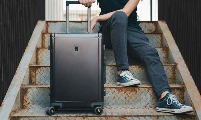 Person sitting on stairs with a black rolling suitcase