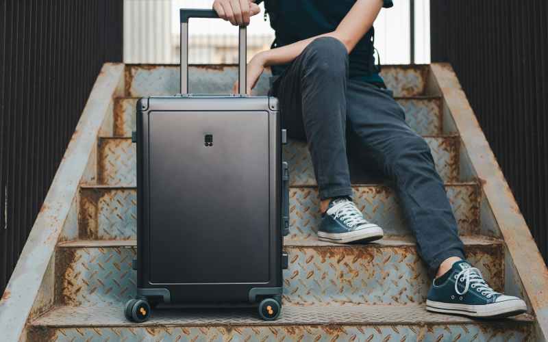 Person sitting on stairs with a black rolling suitcase