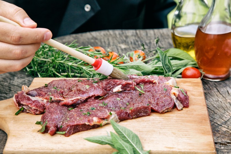 Cooking ingredients: marinated meat,oil,vinegar, herbs and vegetables. Chef is carving and marinating meat