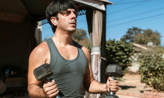 man holding dumbbells sitting on bench outside