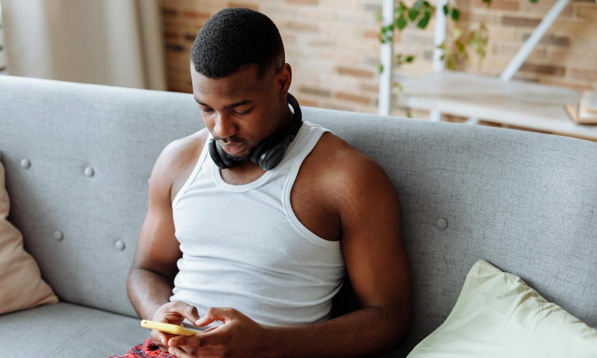 Man sitting on couch wearing headphones relaxing on phone