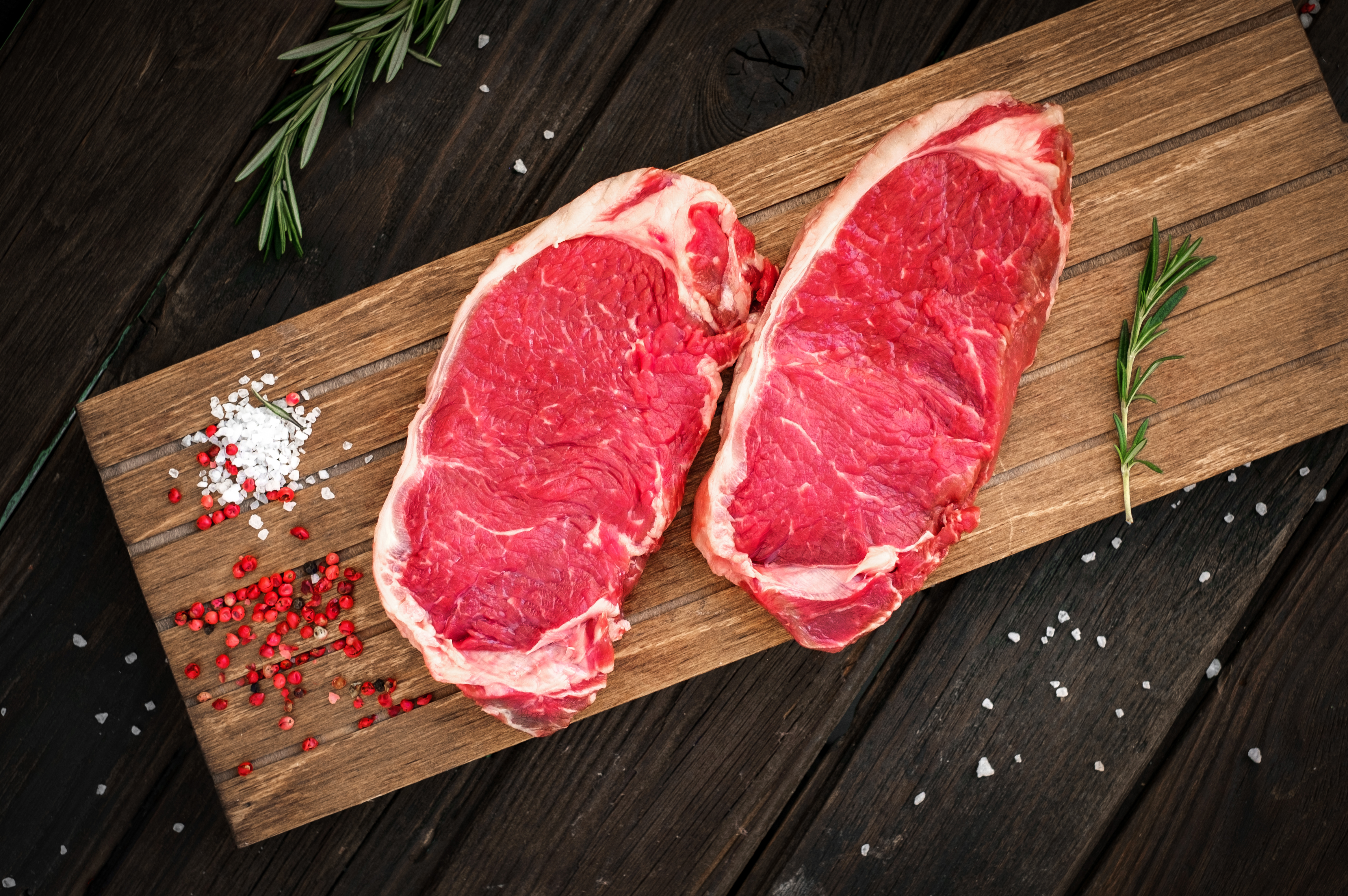 raw sirloin steak being prepared on wooden board