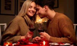 Happy young couple in love clinking glasses drinking wine having romantic dinner date celebrating Valentines Day evening anniversary sitting at table at home or in restaurant. Valentine's Day concept