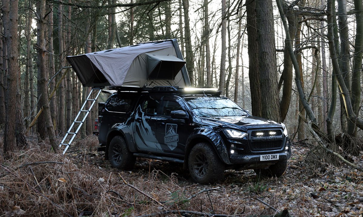 An Isuzu Basecamp truck camper with a rooftop tent setup in the woods.