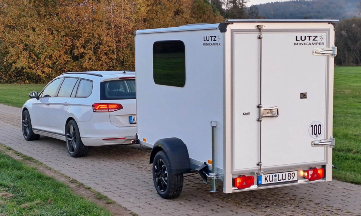 A white Volkswagen wagon towing a Lutz Minicamper travel trailer.