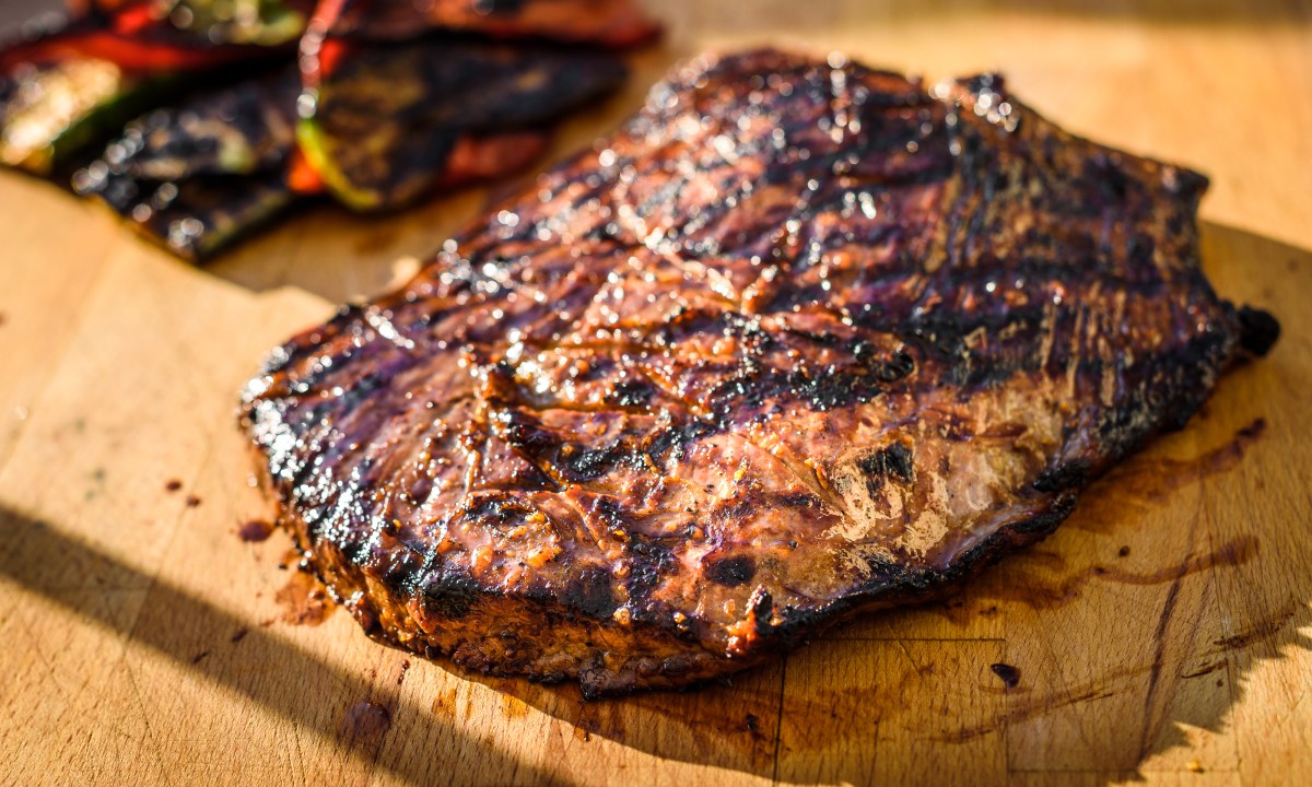 Grilled juicy marinated angus beef flank steak on wooden board. Finished juicy medium rare meat is resting before it is cut and sliced.