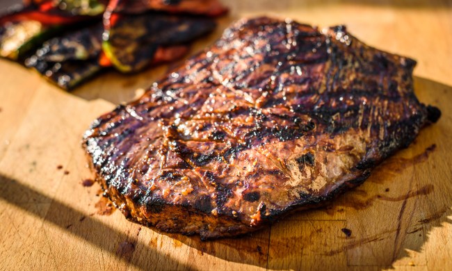 Grilled juicy marinated angus beef flank steak on wooden board. Finished juicy medium rare meat is resting before it is cut and sliced.