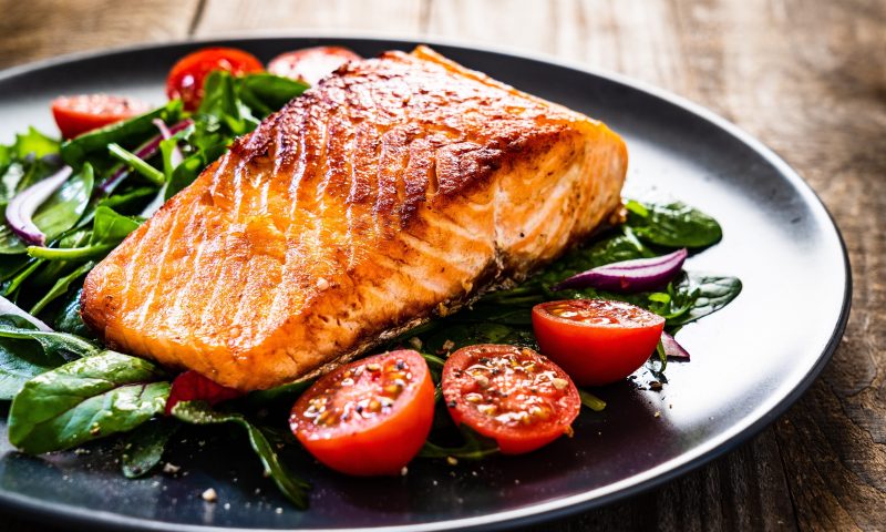 Fried salmon steak with vegetables on wooden table