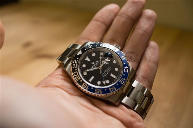 Rolex GMT Master II on a hand in front of a wood grain background.